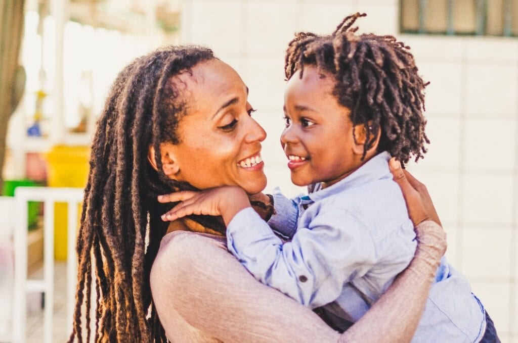 Happiness and joyful  black race african family concept with mother and son together having fun and laughing a lot - hug and love - afro people with dreadlocks hair style - trendy family